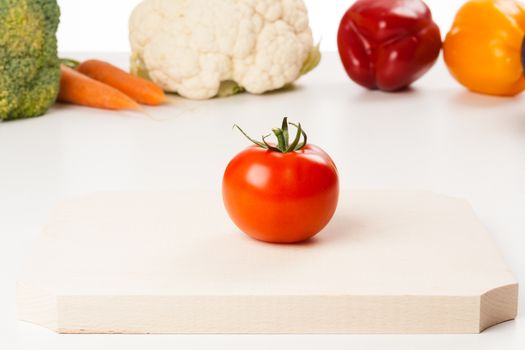 tomato on cutting board with different vegetables in the background