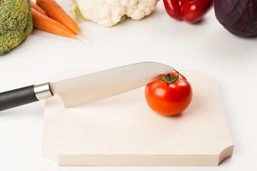 tomato on cutting board with different vegetables in the background