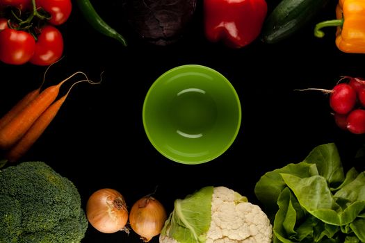 border made of different vegetables with bowl in the middle on black background