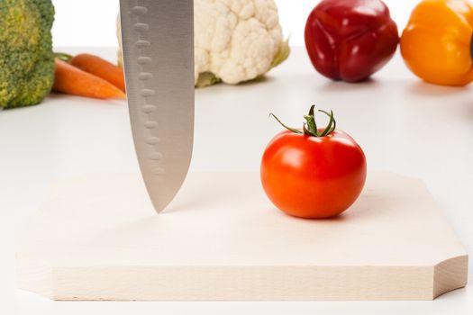 tomato on cutting board with different vegetables in the background