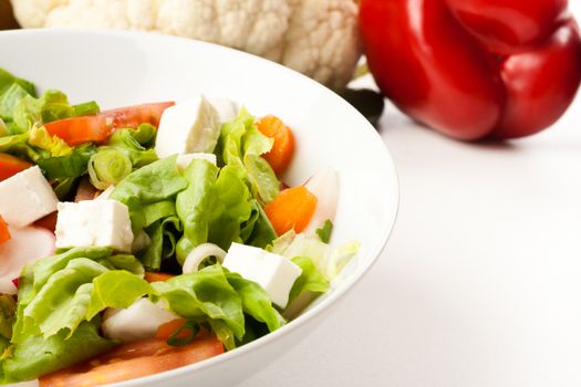 vegetable salad in white bowl with different vegetables in the background