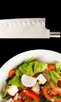 vegetable salad in a white bowl with big knife on black background