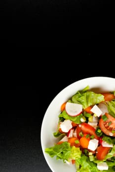 vegetable salad in white bowl on black background