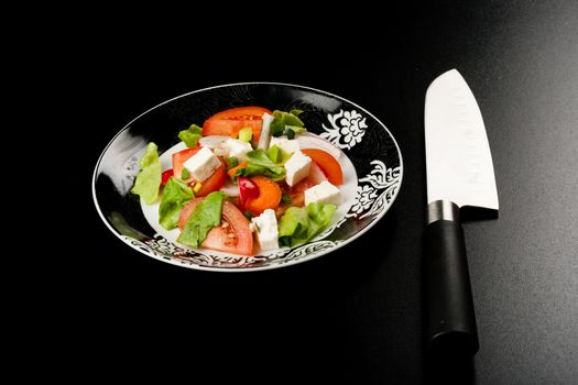 vegetable salad in a white bowl with big knife on black background