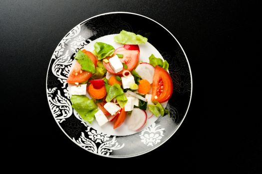 vegetable salad in stylish balck and white plate on black background