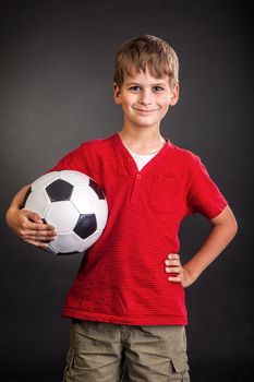 Cute boy is holding a football ball made of genuine leather isolated on a black background. Soccer ball