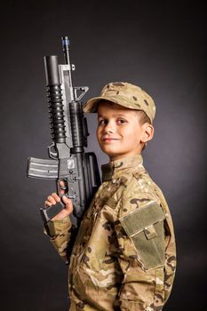 Young boy dressed like a soldier with rifle isolated on black background