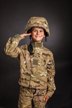 Saluting soldier. Young boy dressed like a soldier isolated on gray background