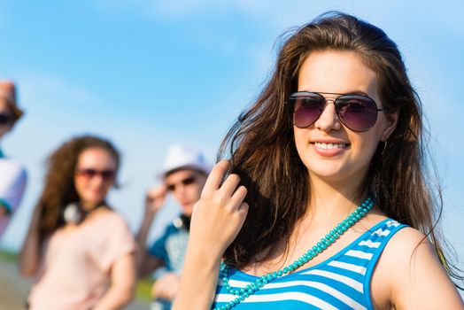 stylish young woman in sunglasses on the background of blue sky and friends