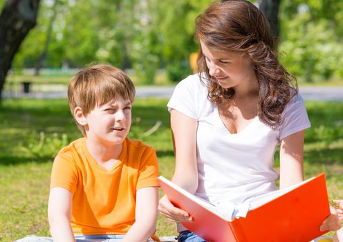 boy and a woman in a summer park reading a book together