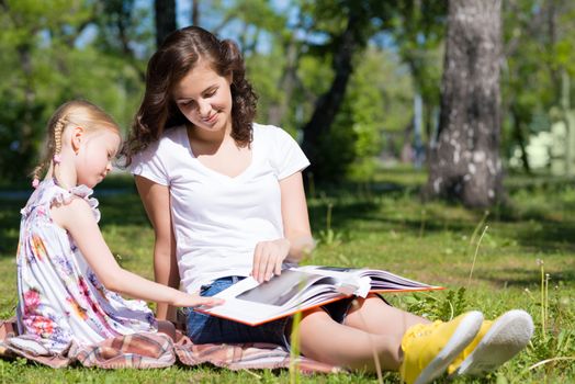 girl with the teacher reading a book together in the summer park