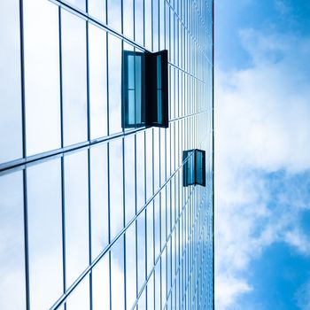 Modern facade of glass and steel with open window reflecting sky and clouds.