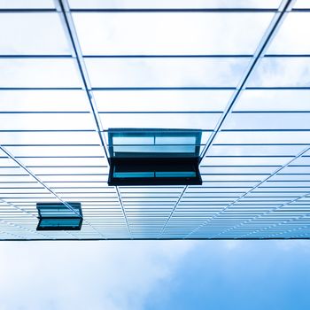 Modern facade of glass and steel with open window reflecting sky and clouds.