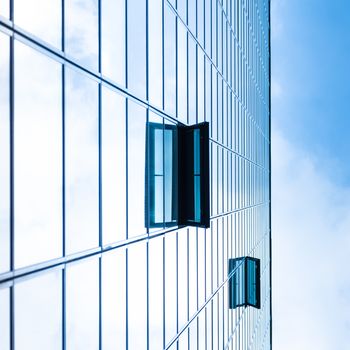 Modern facade of glass and steel with open window reflecting sky and clouds.