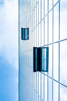 Modern facade of glass and steel with open window reflecting sky and clouds.