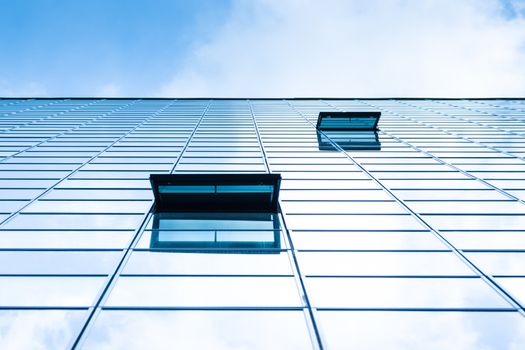 Modern facade of glass and steel with open window reflecting sky and clouds.