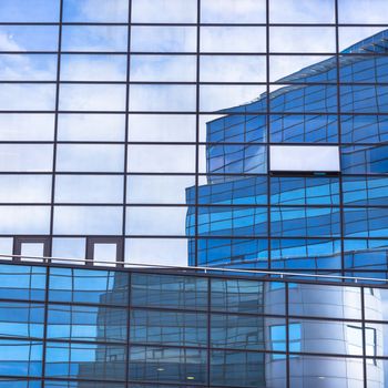 Modern facade of glass and steel with open window reflecting sky and clouds.