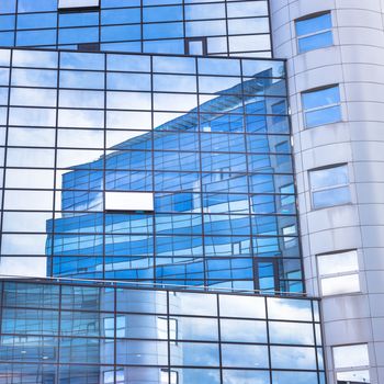 Modern facade of glass and steel with open window reflecting sky and clouds.