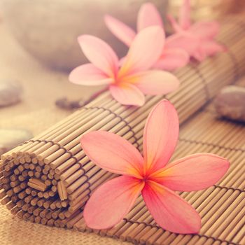 Health spa setting, low light with ambient. Frangipani, hot and cold stone on bamboo mat in vintage retro style.
