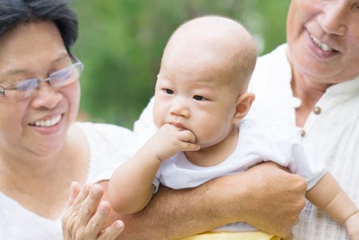 Asian grandparents playing with baby grandchild at outdoor garden.