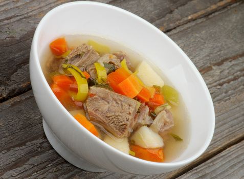 Rustic Beef Soup with Potato, Carrot, Leek and Greens in White Bowl closeup on Wooden background