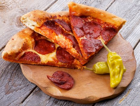 Slices of Tasty Pepperoni Pizza with Two Jalapeno Peppers on Wooden Plate closeup on Rustic Wooden background