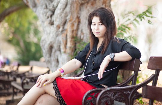 Asian women sitting on a bench. Black shirt sitting in the park.