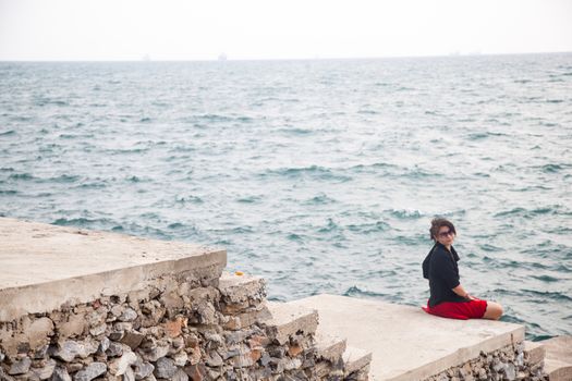 Asian women black shirt. Sitting on the sidewalk. A bridge near the ocean