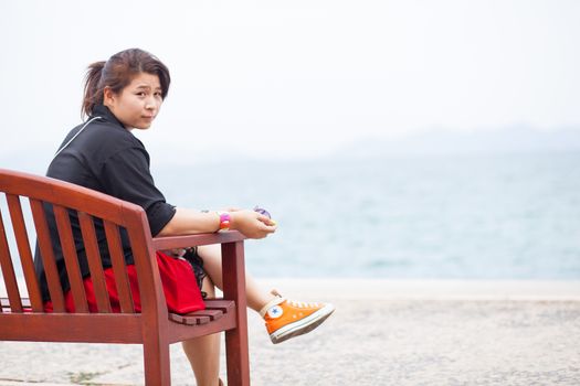 Asian women black shirt. Sitting on wooden bench. Adjacent to the corridor of the park.