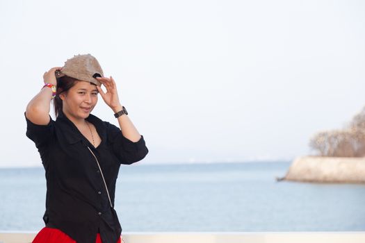 Asian women black shirt. She was wearing a hat In the background is the sea in the evenings.