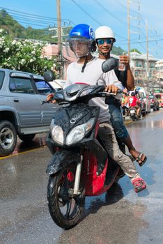 Phuket, Thailand - April 13, 2014: Two Thai on moped drive wet because of  celebration Songkran Festival, the Thai New Year by splashing water to each others on Patong streets. 