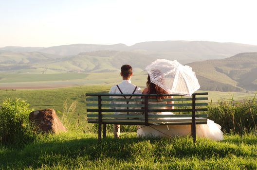 Bride and groom outside garden wedding on bench with African Natal Midlands mountain scenery background