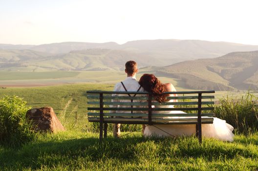 Bride and groom outside garden wedding on bench with African Natal Midlands mountain scenery background