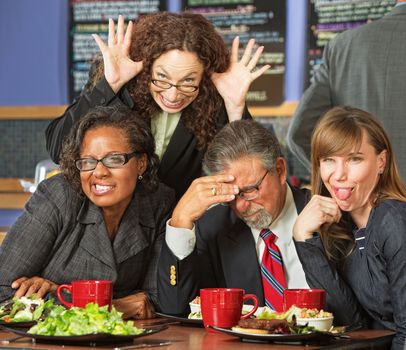 Embarrassed man with coworkers making faces in cafe