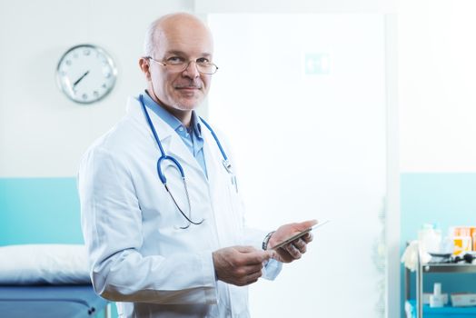 Senior doctor with tablet and medical equipment in the background.