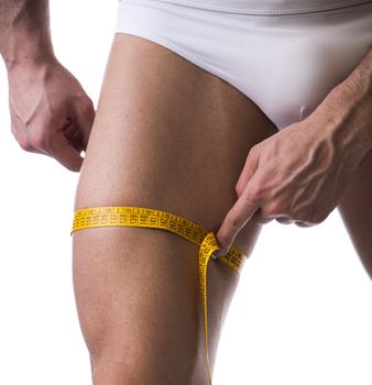 Muscular young man measuring thigh with tape measure, close-up of leg on white background