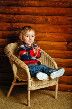 Little boy sitting in a wicker chair in a wooden house