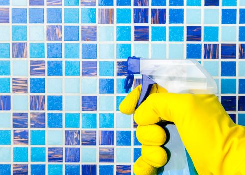 Hand in yellow protective glove holding spray bottle cleaning mosaic wall