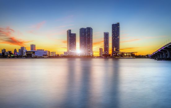 Miami city skyline panorama at dusk with urban skyscrapers over sea with reflection 