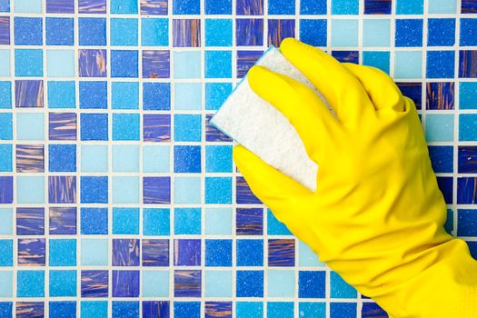 Hand in yellow protective glove cleaning mosaic wall with sponge