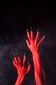 Horror red devil hands with black nails on smoky background, studio shot 