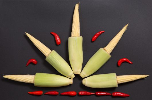 Fresh raw baby corn cobs with red non-stem chili peppers on gray background 