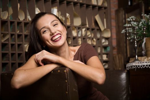 Young woman sits in an armchair on a background of vintage interior.