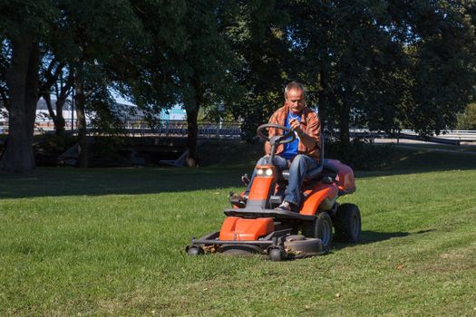 man driving a lawn mower in the city park