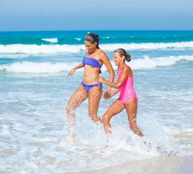 Cute girls friends running together in the beach shore on summer vacation