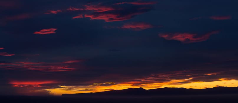 Panoramic sunset over the coast of New Zealand as the sun illuminates the clouds with brilliants reds and oranges with the ocean providing foreground