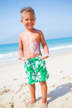 Adorable boy at tropical beach with sunblock cream.