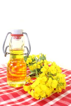 a bottle of rapeseed oil and rapeseed flowers against white background