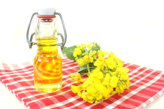 a bottle of rapeseed oil and rapeseed flowers against white background