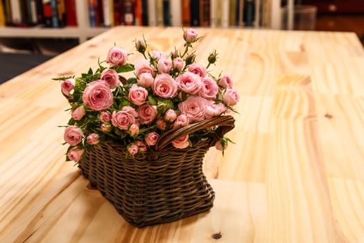 Bunch of small pink Roses in a basket over a wooden table.
